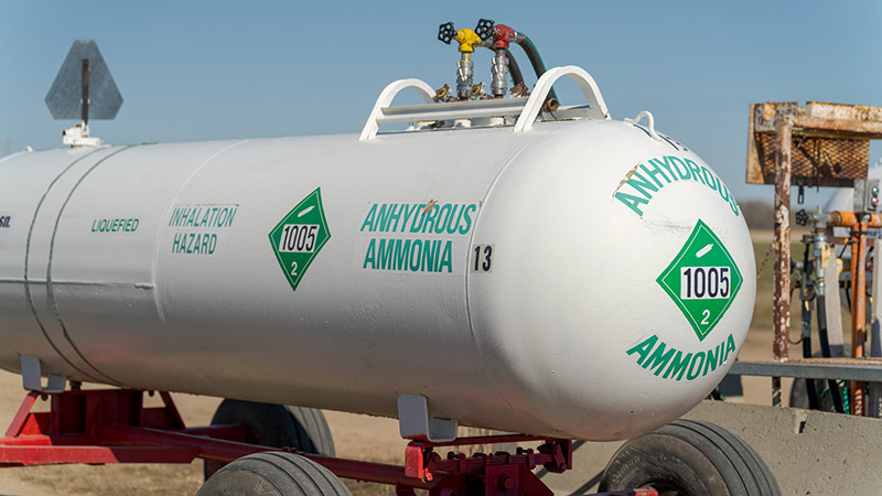 White anhydrous ammonia nurse tank on a red wagon frame, marked with green UN 1005 hazard placards