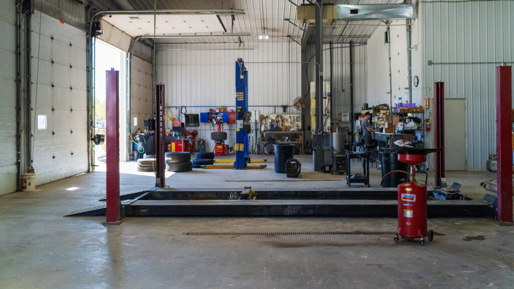Inside the Middle River Co-op Oil service shop, with a four-post drive-on lift, a two-post lift, and stacked tires
