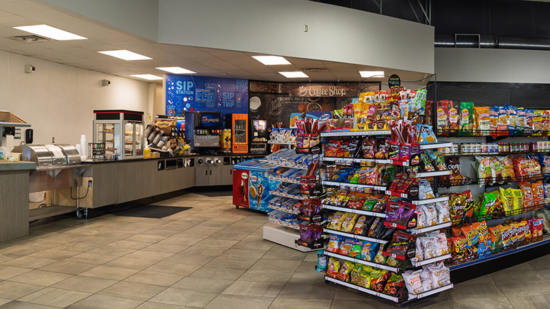 Snack aisle and endcap displays inside the Middle River Co-op Oil store, with the coffee shop in back