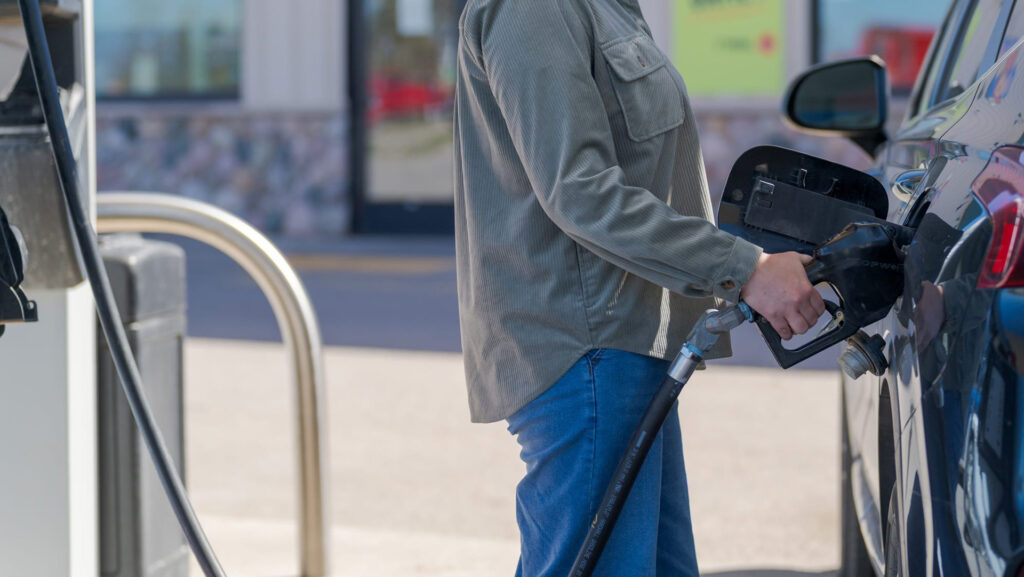 Customer pumping gas into a dark blue car at a fuel pump outside the convenience store